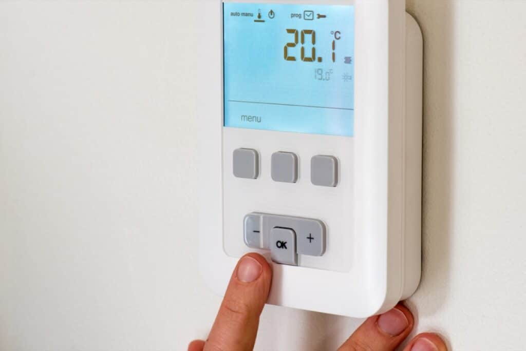 Hand stelt een digitale kamerthermostaat in op 20 graden